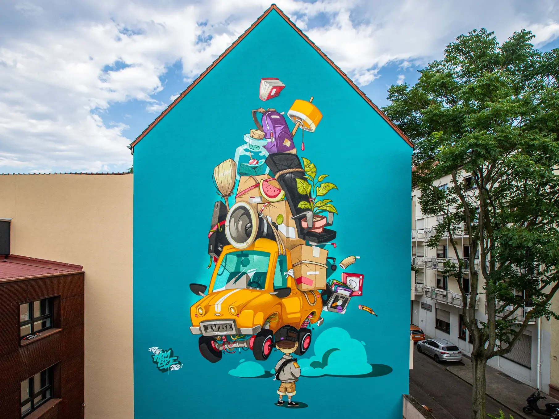 KI-basierte Bildbeschreibung: Eine farbenfrohe Wandmalerei an einer hohen Gebäudewand zeigt ein Cartoon-Kind, das zu einem gelben Auto hinaufschaut, das mit verschiedenen Gegenständen überfüllt ist, darunter Pflanzen, Elektronik und Möbel, die alle hoch gestapelt sind und über dem Auto balancieren.
