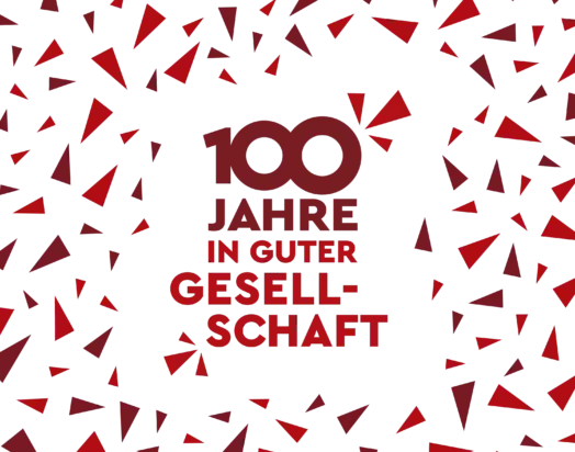 KI-basierte Bildbeschreibung: Der Text „100 Jahre in guter Gesellschaft“ in fetter roter Schrift auf weißem Hintergrund, umgeben von verstreuten roten und kastanienbraunen geometrischen Dreiecken.
